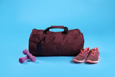 Kırmızı spor çantası, spor ayakkabıları ve açık mavi arka planda dambıllar.