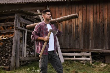 Baltalı ve kütüklü bir adam dışarıda odun yığınının yanında.