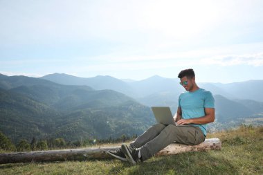 Güneşli bir günde dağlarda dizüstü bilgisayarla çalışan bir adam.