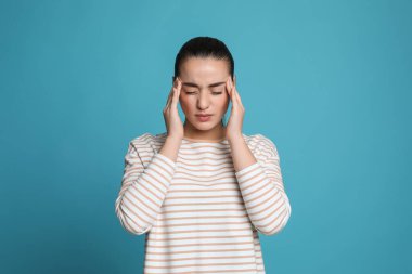 Açık mavi arka planda baş ağrısı çeken genç bir kadın.