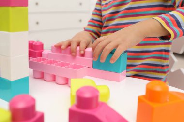Şirin küçük kız renkli yapı taşlarıyla oynuyor. Masanın içinde, yakın planda.
