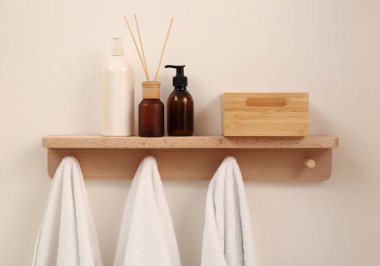 Havluları, sabunlukları ve bej duvarında aromatik kamış spreyi olan ahşap bir raf. İç öge