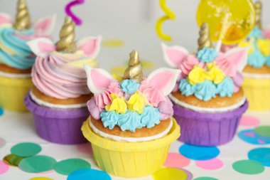 Tatlı tatlı tek boynuzlu at kekleri ve beyaz masada şenlikli bir dekor.