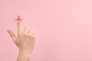 Pembe arkaplanda hatırlatma olarak bağlı kırmızı yay ile işaret parmağı gösteren kadın, yakın plan, metin için boşluk