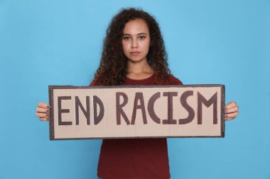 Afro-Amerikalı kadın açık mavi arka planda ırkçılığı sona erdirme tabelası taşıyor