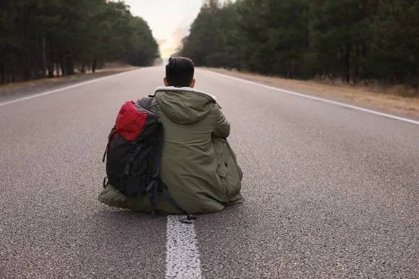 森の近くの道路に座ってバックパックを持つ男は ビュー — ストック写真