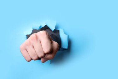 Adam açık mavi kağıdı yumrukla delip geçiyor, yakın plan. Metin için boşluk