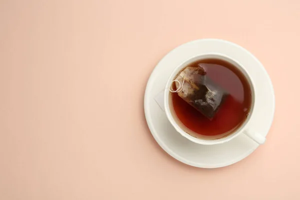 Tea bag in cup of hot water on pink background, top view. Space for text