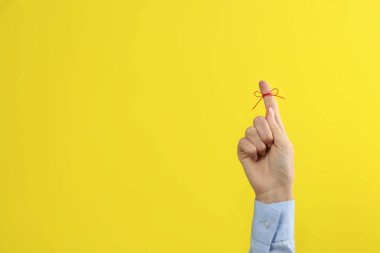 Sarı arka planda bağlı kırmızı fiyonklu işaret parmağı gösteren kadın, yakın plan. Metin için boşluk