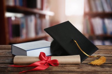 Mezuniyet şapkası, kitap ve diploması kütüphanedeki ahşap masada.