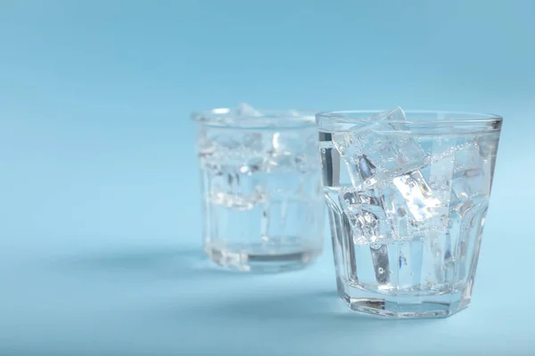Glasses of soda water with ice on light blue background. Space for text
