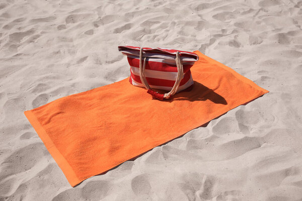 Soft orange beach towel and bag on sand