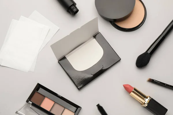 Flat lay composition with facial oil blotting tissues and makeup products on light grey background. Mattifying wipes