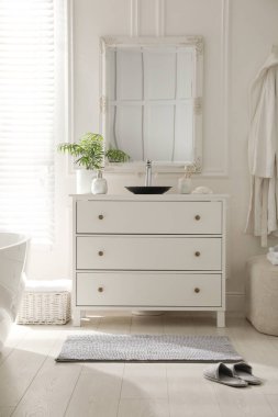 Şık gri paspas ve banyo çekmecesinin yanındaki terlikler.