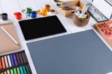 Boş kağıt, renkli tebeşirli pasteller, tablet ve diğer çizim araçları beyaz ahşap masa üzerinde. Modern sanatçının çalışma yeri