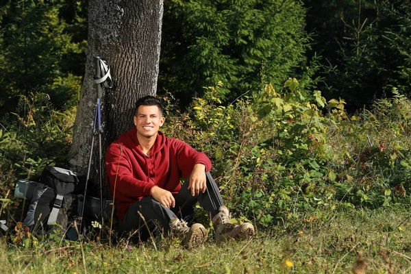 草の上に木の近くに座っているバックパックとトレッキングポール付きのハイカー 休憩所 — ストック写真