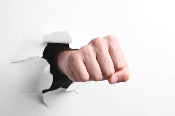 Man breaking through white paper with fist, closeup