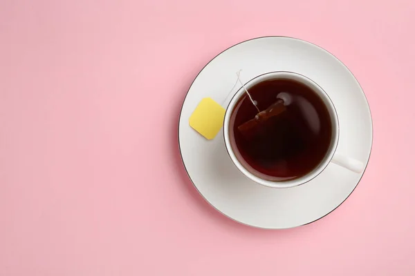 Tea bag in cup of hot water on pink background, top view. Space for text