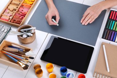 Beyaz ahşap masadaki gri kağıda tebeşirle pastel çizen sanatçı.
