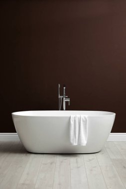Modern seramik banyo küveti. Kahverengi duvarın yanında havlu var.
