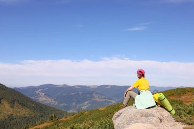 Sırt çantalı genç bir kadın kayalık zirvede, arka planda.
