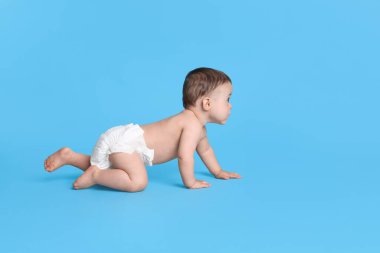 Kuru, yumuşak bezli, açık mavi arka planda emekleyen şirin bir bebek.