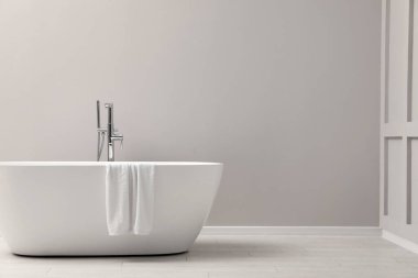 Modern seramik banyo küveti, havluyla birlikte içerisi aydınlık duvar, metin için yer.