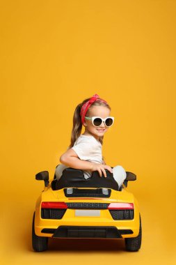 Sarı arka planda çocukların elektrikli oyuncak arabasını kullanan tatlı küçük kız.