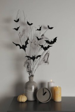 Alarm saati, yanan mumlar ve beyaz duvarın yanındaki masada kağıt sopalarla vazo. Cadılar Bayramı Dekorasyonu