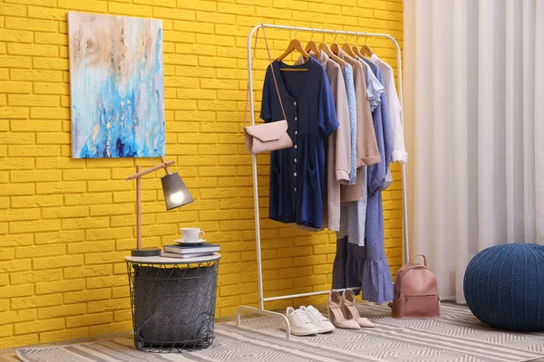 部屋の黄色のレンガの壁の近くに別のスタイリッシュな服や靴を持つラック — ストック写真