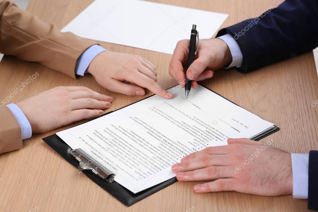 Businesspeople signing contract at wooden table, closeup of hands