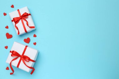 Güzel hediye kutuları ve açık mavi arka planda kırmızı dekoratif kalpler, düz yatış. Metin için boşluk