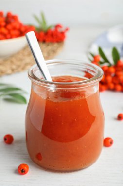 Cam kavanozdaki leziz rowan reçeli beyaz ahşap masada.