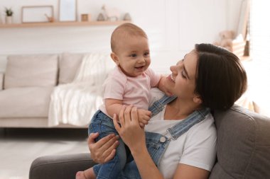 Mutlu bir genç anne ve sevimli bebeği evde koltukta oturuyor.