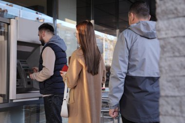 Genç adam para çekmek için para makinesini açık havada kullanıyor. ATM kuyruğu