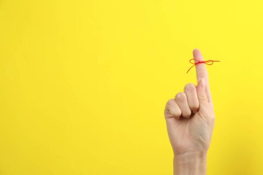 Sarı arka planda bağlı kırmızı fiyonklu işaret parmağı gösteren kadın, yakın plan. Metin için boşluk