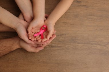 Ahşap arka planda pembe kurdeleli bir aile, yazı için geniş manzaralı bir yer. Göğüs kanseri farkındalığı