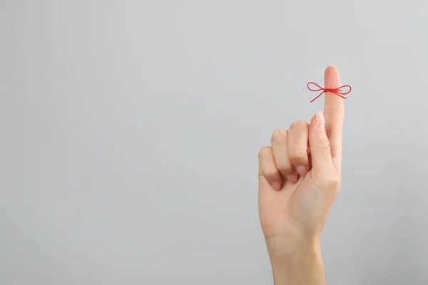 Woman showing index finger with tied red bow as reminder on light grey background, closeup. Space for text