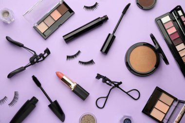Mor arka planda kirpik bigudileri ve makyaj ürünleri düz yatıyordu.