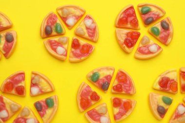 Sarı arka planda pizza şeklinde lezzetli jöle şekerler, düz uzanmış.