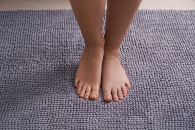 Yumuşak gri banyo paspasının üzerinde duran kadın, yakın plan.