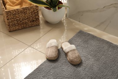 Yumuşak gri banyo paspası ve yerde terlikler.