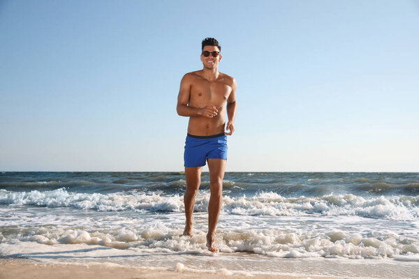 Handsome man with attractive body running on beach