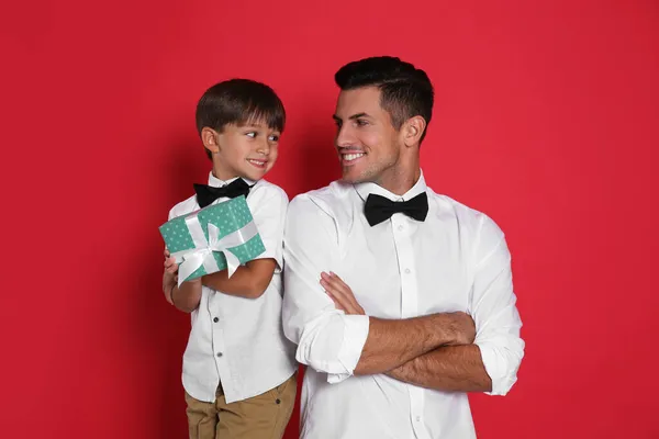 Man receiving gift for Father's Day from his son on red background