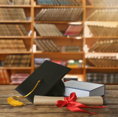 Mezuniyet şapkası, kitap ve diploması kütüphanedeki ahşap masada.