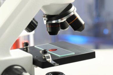 Laboratuvarda mikroskop altında kırmızı sıvı numunesiyle cam kaydırma, yakın plan.