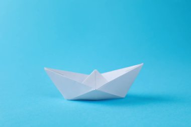 Açık mavi arka planda el yapımı beyaz kağıt tekne. Origami sanatı