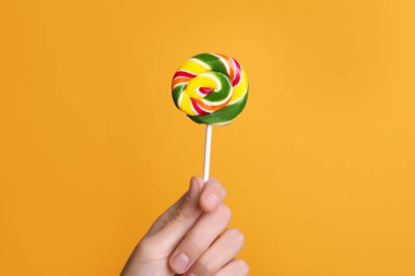 Turuncu arka planda parlak, lezzetli lolipop tutan kadın, yakın plan.