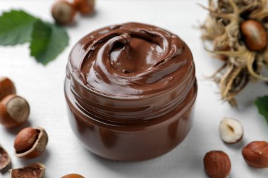 Lezzetli çikolata soslu cam kavanoz ve beyaz ahşap masada fındık.