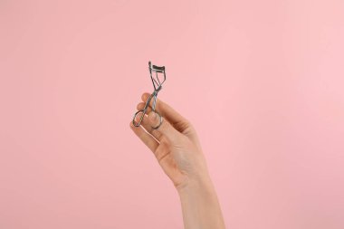 Pembe arka planda kirpik bigudisi tutan kadın, yakın plan. Makyaj aracı